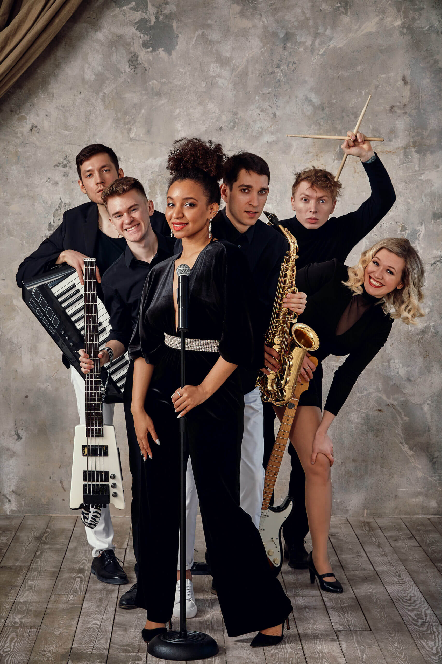 Gruppe von Menschen mit Musikinstrumenten posiert vor einer Betonwand.