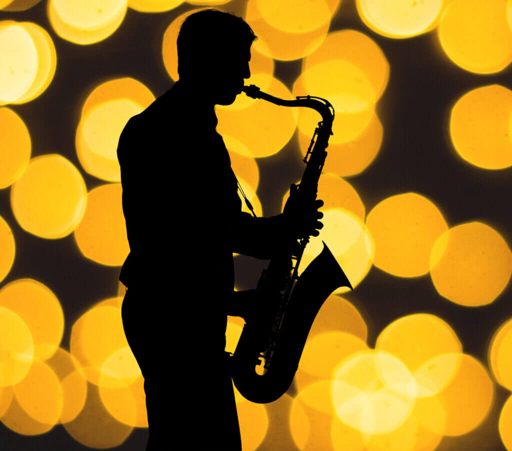 Silhouette eines Saxophonspielers vor gelbem Lichtbokeh.